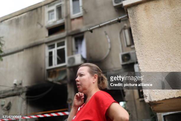 October 2023, Israel, Ashkelon: A woman stands in front of a damaged residential building which was hit by rockets fired from Gaza in the aftermath...