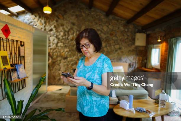 カジュアルなスウェットシャツを着たアジアの70歳の女性が、思慮深い表情で携帯電話のメッセージを見て、指で返信を入力しています - 65 year old asian women ストックフォトと画像