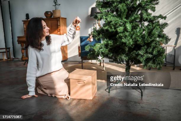 adding christmas charm: elegant lady adorns christmas tree with wooden house featuring a heart - moment of silence stock-fotos und bilder