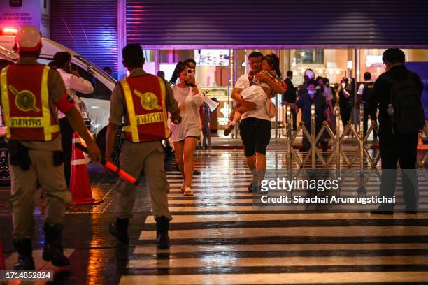 People carry a sleeping child as they exit the Siam Paragon mall as a shooting incident was still ongoing inside on October 03, 2023 in Bangkok,...