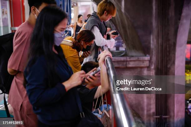 People stand near the Siam Paragon mall after being evacuated from the Paragon after a shooting incident inside on October 03, 2023 in Bangkok,...