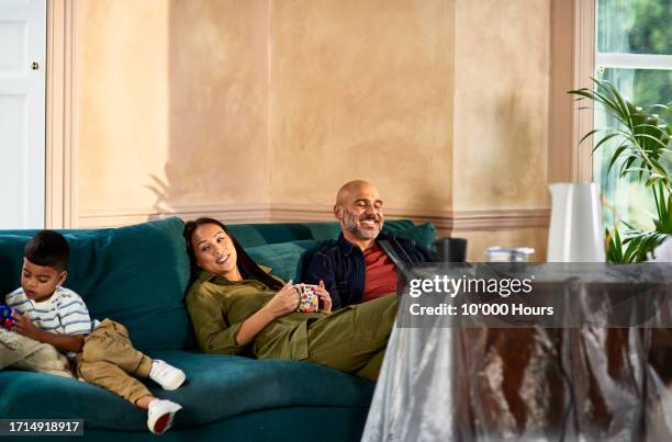 boy lying on sofa with parents relaxing with mug of coffee tired after moving day - afterr stock pictures, royalty-free photos & images