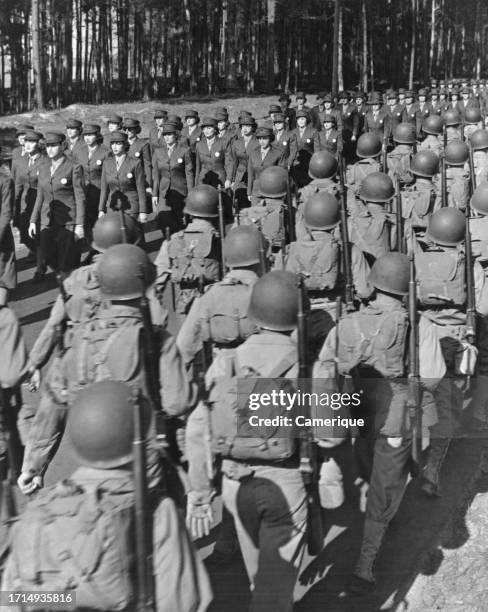 Rows of Marines in full battle garb with guns, helmets and backpacks marching in one direction as female Marines in formal uniform march the opposite...