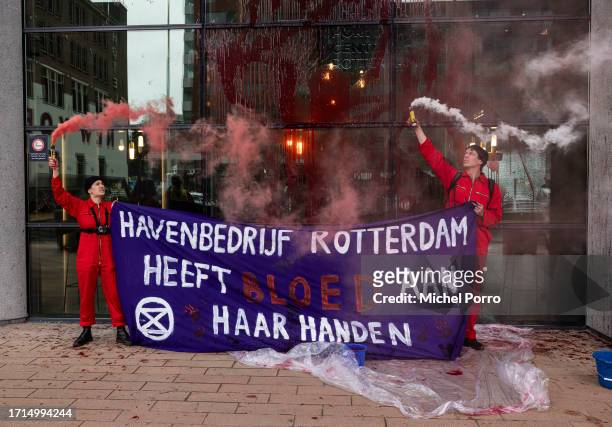 Protestors holding a banner that reads 'Harbour Rotterdam has blood on her hands' throw red paint over the windows of the Rotterdam Harbour office in...