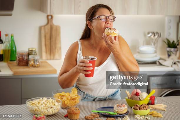 donna avida che si diverte a mangiare una ciambella e bere cola. concetto di alimentazione malsana - fat people eating donuts foto e immagini stock