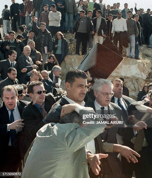 Bodyguards hold an anti-bullet shield over French Prime Minister Lionel Jospin while he is led away from Palestinian demonstrators into his limousine...