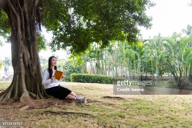young woman reading book under a tree - under skirt stock pictures, royalty-free photos & images