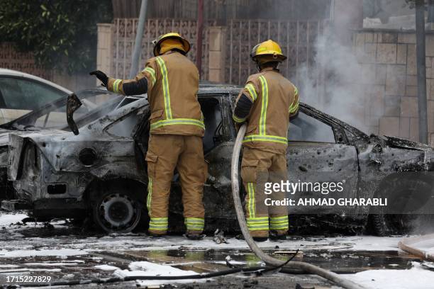 Firefighters extinguish a flame in a car in the southern Israeli city of Ashdod on October 9 after rockets fired from Gaza landed in the city. Israel...