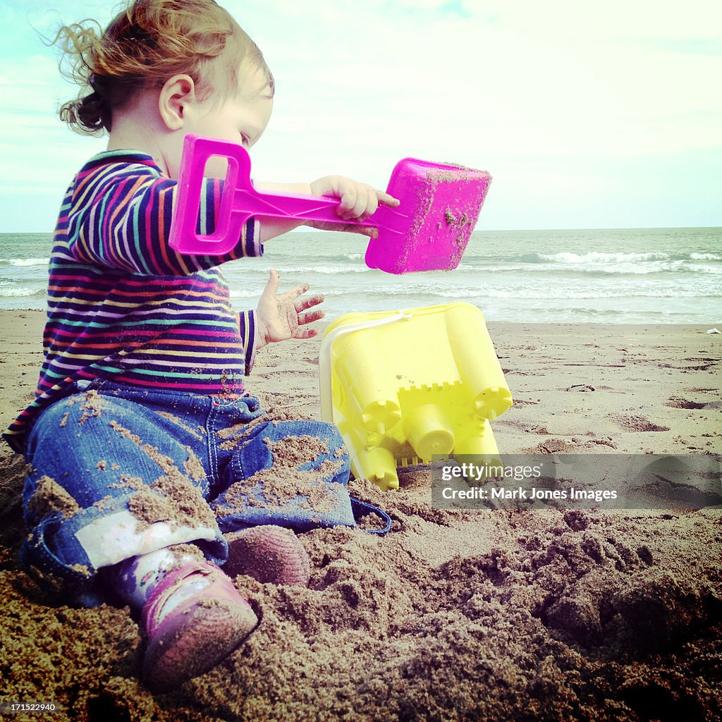 Toddler using bucket and spade on beach by sea