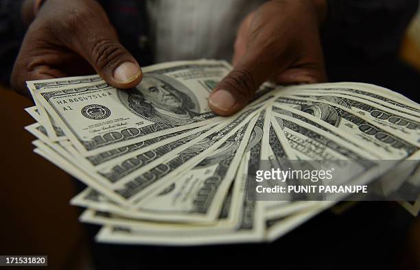 An Indian man displays US dollar notes at a local currency exchange shop in Mumbai on June 26, 2013. India's rupee touched a record low of more than...