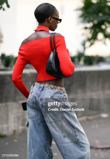 Model is seen wearing a red sweater crop top, blue jeans, light blue and gold belt, black bag and black sunglasses outside the Zimmermann show during...