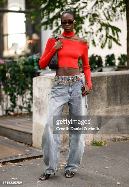 Model is seen wearing a red sweater crop top, blue jeans, light blue and gold belt, black bag and black sunglasses outside the Zimmermann show during...