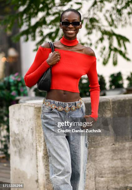 Model is seen wearing a red sweater crop top, blue jeans, light blue and gold belt, black bag and black sunglasses outside the Zimmermann show during...