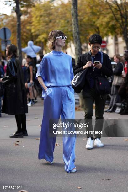 Anya Ziourova wears sunglasses, a blue / purple shiny / silk / lustrous top, matching palazzo flared pants, outside Miu Miu, during the Womenswear...