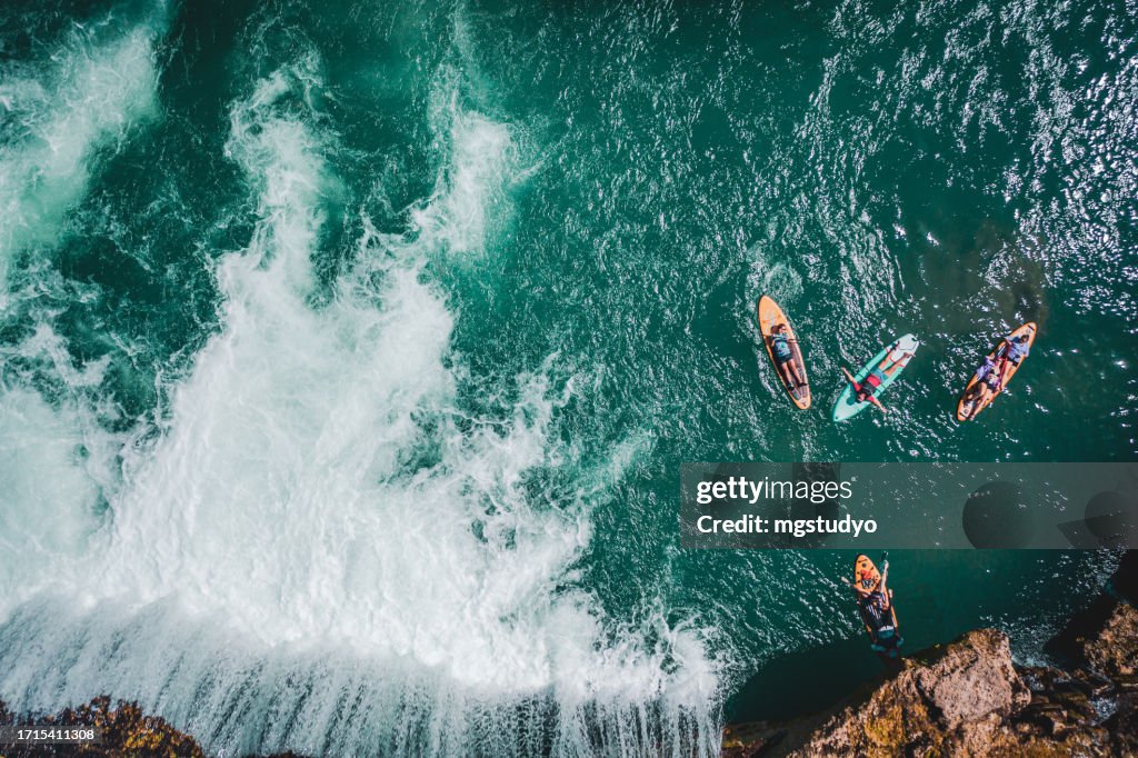 Aerial view of Group of friends paddle boarding together by waterfall.