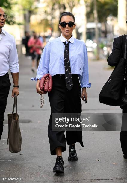 Jeannie Lee is seen wearing a light blue and white collar shirt, blue print tie, black pants, black Prada shoes, pink and gold chain bag and black...