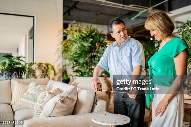 mature couple talking while measuring a table at the furniture store - happiness meter stock pictures, royalty-free photos & images