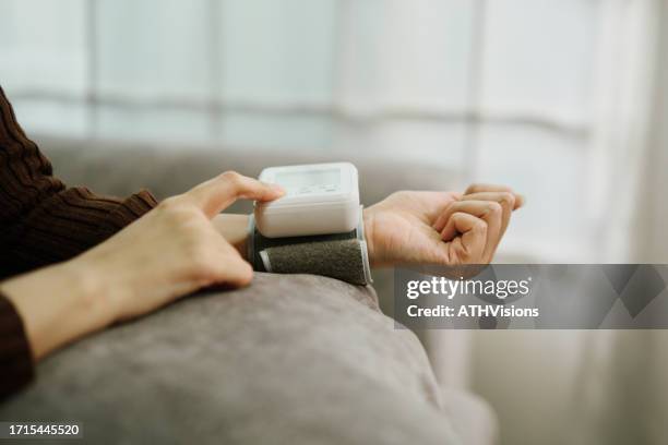 compromiso con el bienestar: una mujer adulta enferma controla la presión arterial - dispositivo de control fotografías e imágenes de stock
