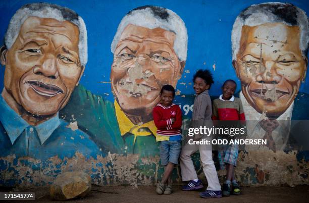 Children pose in front of a mural of Nelson Mandela in Soweto on June 26, 2013. Mandela is receiving treatment at the Mediclinic heart hospital in...