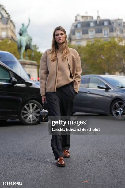 Zita D'Hauteville wears a pale / pastel brown / beige Miu Miu wool cardigan, a pullover, black pants, a black leather bag, brown leather shoes ,...