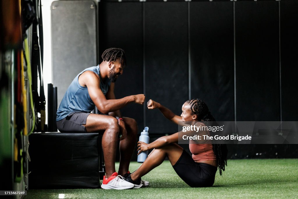 Young man giving fist bump to female friend at gym