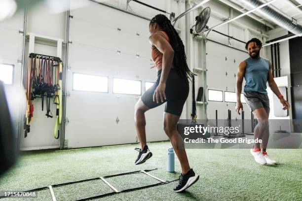 happy man looking at woman exercising on agility ladder in health club - agility ladder stock-fotos und bilder