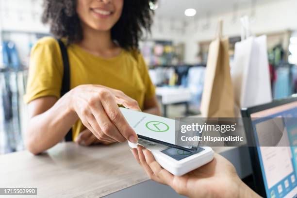 mujer haciendo un pago móvil en una tienda de ropa - marca de pago por móvil fotografías e imágenes de stock