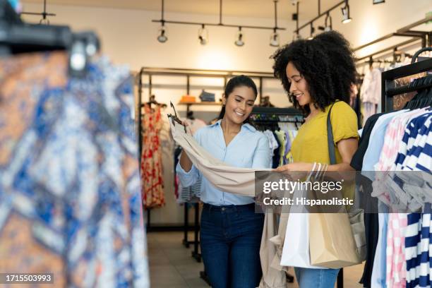 woman shopping at a clothing store with the help of a saleswoman - kledingwinkel stockfoto's en -beelden