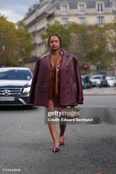 Paola Locatelli wears a necklace, an orange wool mini dress, a brown leather jacket, a burgundy leather texture oversized jacket, a brown Miu Miu...