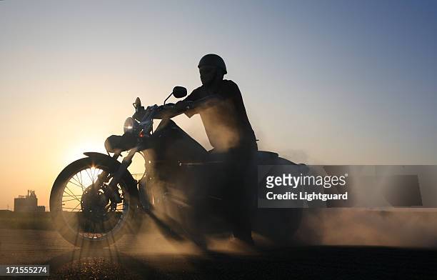smoking motorbike and rider sillhouetted against blue prairie sky - motorbike ride stockfoto's en -beelden