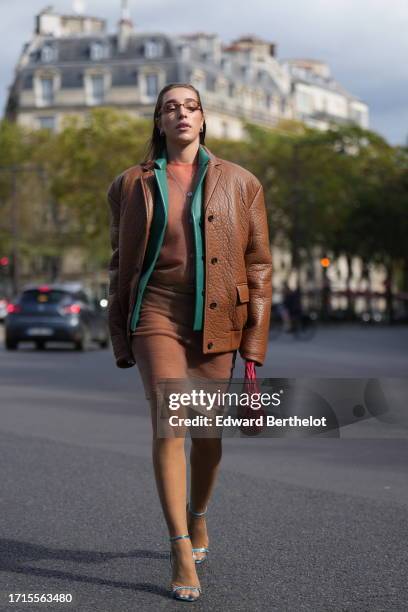 Ginevra Mavilla wears sunglasses, an orange cardigan, a matching ribbed on-knee skirt, a green leather jacket, a brown leather thick oversized...