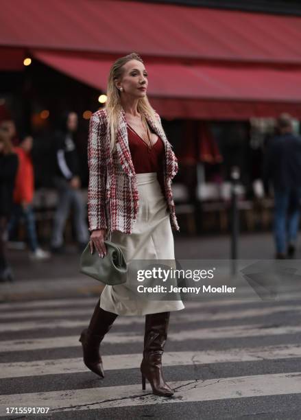 Anna Wohlthat is seen wearing pearl earrings, a red/creme-white checked tweed blazer, underneath a red top, a silver ring with green gemstone, a...