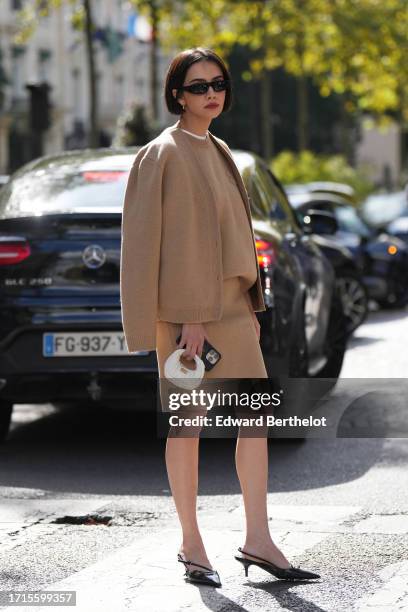 Guest wears sunglasses, a beige pastel / pale brown full look, cardigan, wool pupllover, white t-shirt, mini skirt, a white mini bag, pointed shoes,...