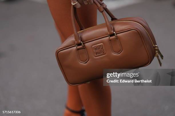 Guest holds a brown leather rectangle shaped bag from Miu Miu , outside Miu Miu, during the Womenswear Spring/Summer 2024 as part of Paris Fashion...