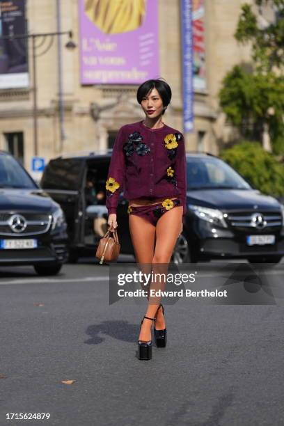 Molly Chiang wears earrings, a purple floral print cardigan, matching underwear, a brown leather rectangular bag, platform shoes, outside Miu Miu,...