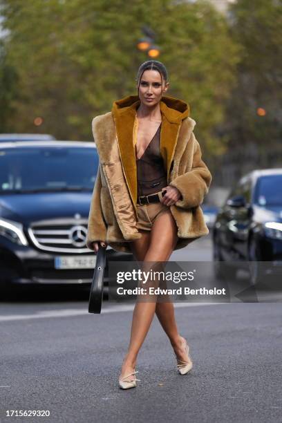 Sabina Jakubowicz wears a brown fluffy oversized coat with hood, a black mesh low-neck top, a belt, mini corduroy shorts, a black Coperni leather...