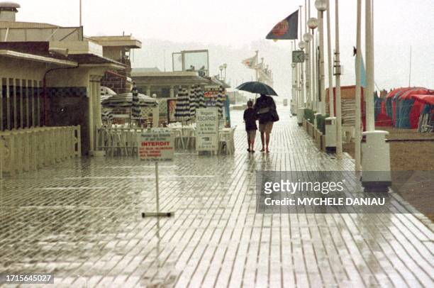 Un père et son enfant se protègent le 02 août sous un grand parapluie pour regagner leur voiture alors qu'il pleut sur les celebres planches de...