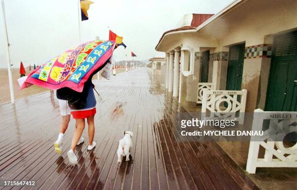 Un couple de vacanciers se protège de la pluie à l'aide d'une serviette de plage, le 02 août, sur les célèbres planches de Deauville désertées en...