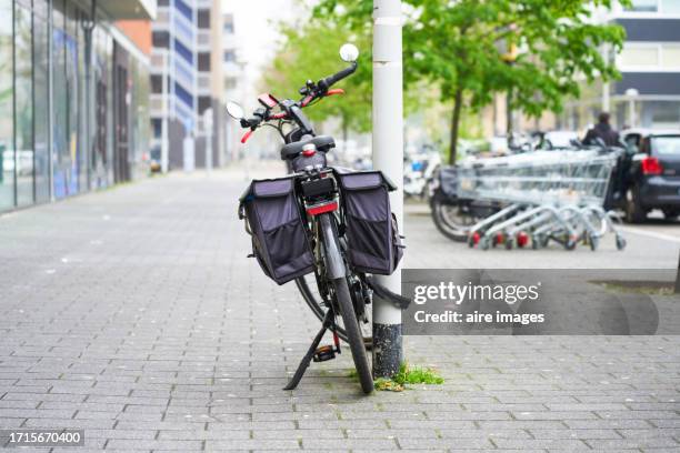 bicycle with backpacks on its sides parked on a light pole on the sidewalk outside a building, rear view - poteau dappui photos et images de collection