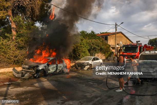 People douse a car blaze in the southern Israeli city of Ashkelon after a rocket attack from Gaza on October 9, 2023. Stunned by the unprecedented...