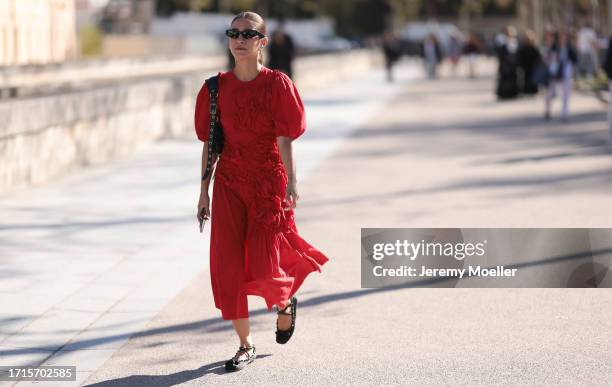 Fashion Week Guest is seen wearing a long red dress with ruffles and flowers, black ballet flats, a black studded leather le Cagole handbag by...