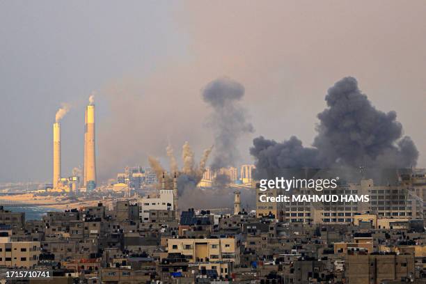 Smoke billows behind highrise buildings in Gaza City during Israeli air strikes on October 9 with the Rutenberg power station, north of the border...