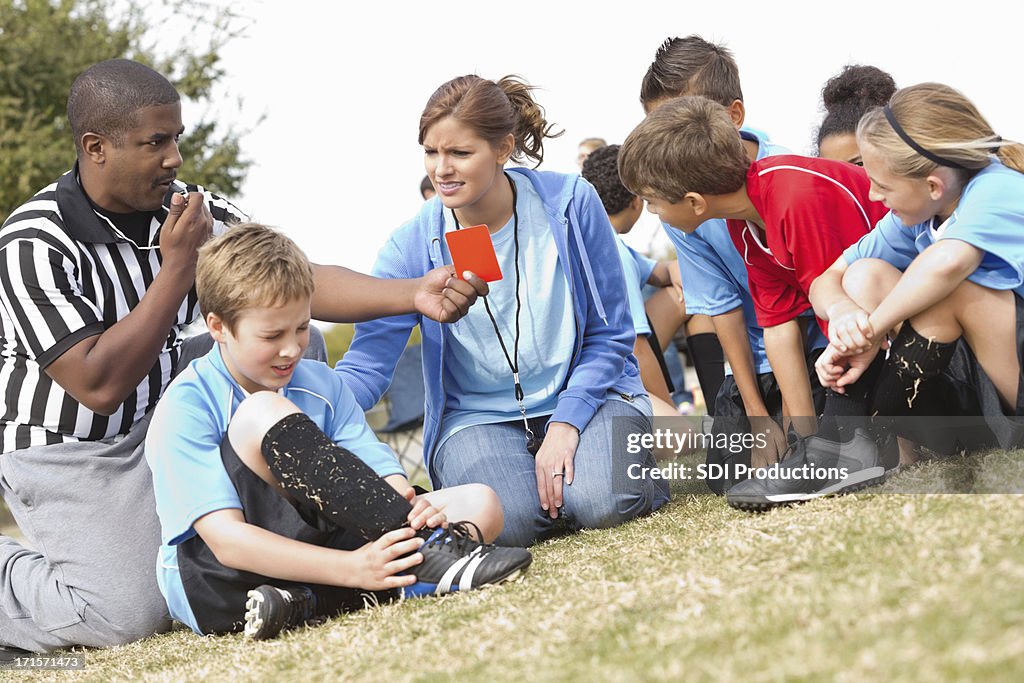 Referee and coach helping injured soccer player during kids' game