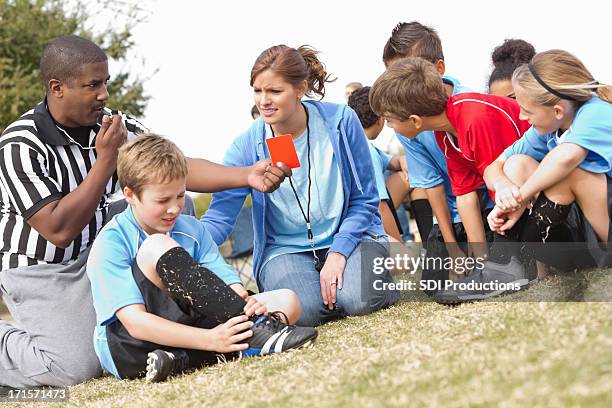 referee and coach helping injured soccer player during kids' game - angry coach stock pictures, royalty-free photos & images