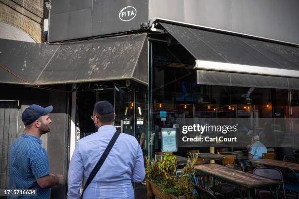 People stand outside a Jewish-owned restaurant that had a glass door smashed in overnight, on October 9, 2023 in the Golders Green area of London,...