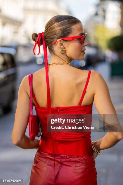 Nina Sandbech wears hair band, golden necklace, red cut out top, bag, leather pants, sunglasses outside during the Womenswear Spring/Summer 2024 as...