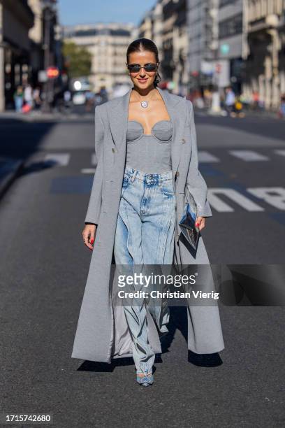 Nina Sandbech wears grey coat, off shoulder top, necklace, sunglasses, denim jeans, blue heels, silver bag outside during the Womenswear...