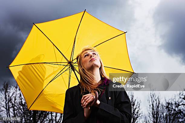 unhappy young woman with umbrella waits for storm to pass - yellow umbrella stock pictures, royalty-free photos & images