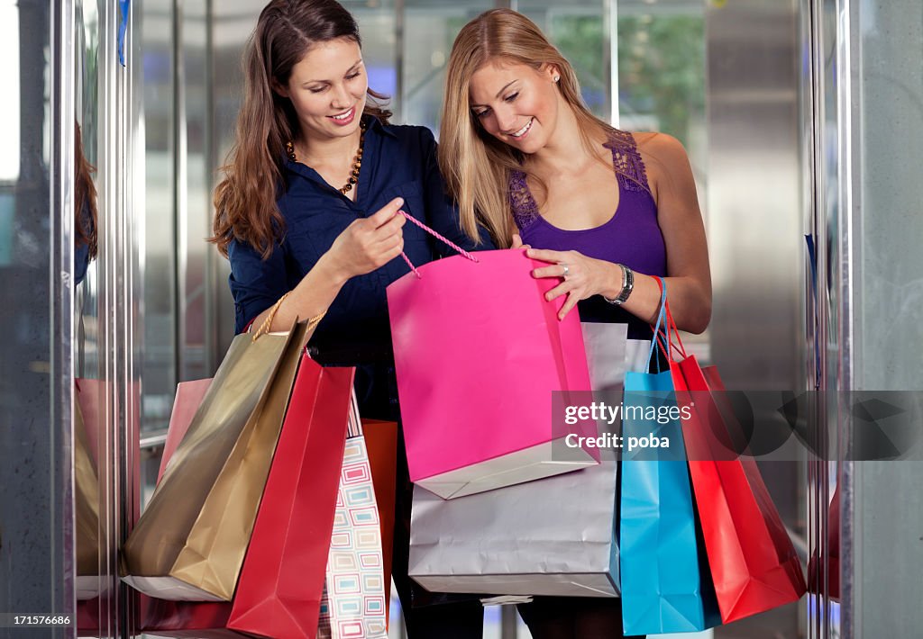 Two girls standing in an elevator and  checking  purchased goods