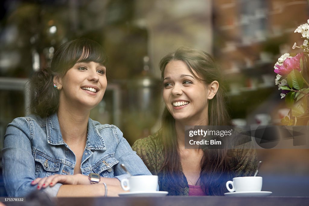 Two Beautiful Women Sitting in Cafe, Smiling, View Through Glass